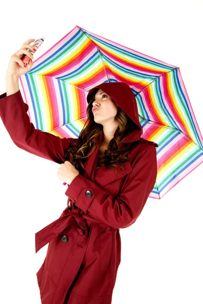 Mujer atractiva en impermeable rojo tomando una foto selfie mientras sostiene un paraguas colorido —  Fotos de Stock