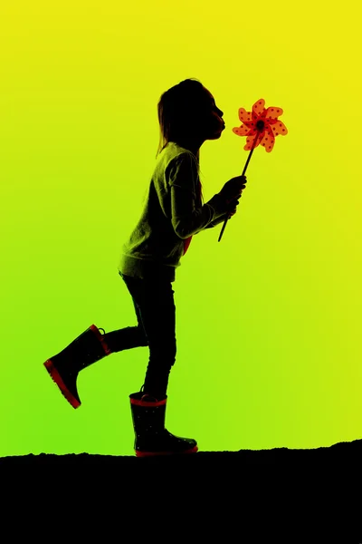 Silhouette of girl walking blowing a toy pinwheel greeen backgro — Stock Photo, Image