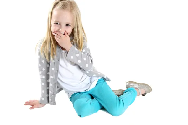 Cute blond girl sitting hand to mouth laughing — Stock Photo, Image