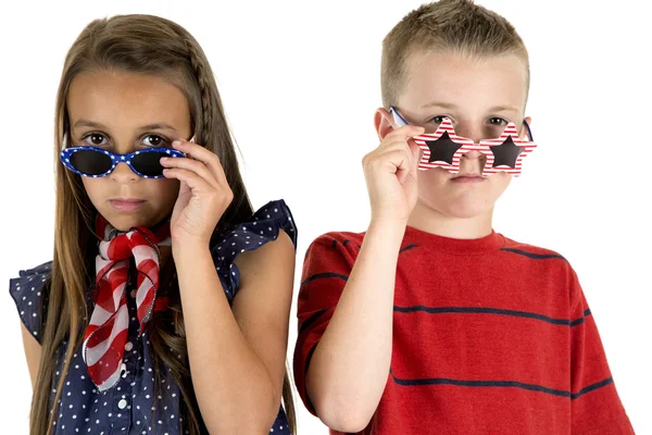 Linda chica y niño mirando por encima de las gafas patrióticas estadounidenses — Foto de Stock