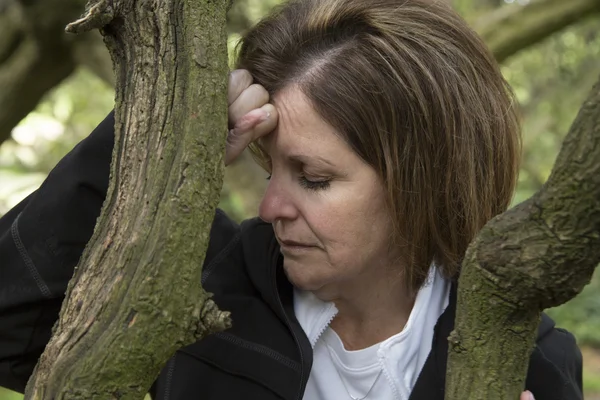 Mulher de meia-idade deprimida na floresta apoiada em uma árvore — Fotografia de Stock