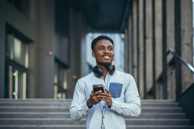 Kazanmaktan mutlu olan genç Afrikalı Amerikalı adam telefondaki sevinçlere ve günlük kıyafetlerdeki gülümsemelere bakıyor.