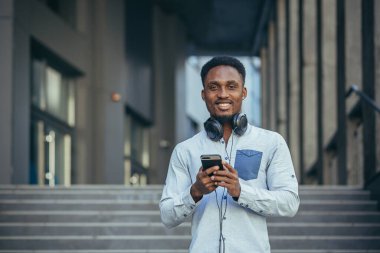 Kazanmaktan mutlu olan genç Afrikalı Amerikalı adam telefondaki sevinçlere ve günlük kıyafetlerdeki gülümsemelere bakıyor.