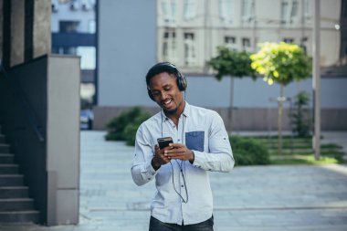 Müzik dinleyen adam büyük kulaklıklar kullanıyor, sokakta yürüyor, mutlu Afro-Amerikan.