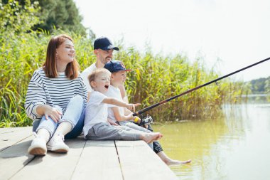 Genç aile, kadın erkek ve iki küçük çocuk gölde balık tutuyor, karı koca birlikte mutlu bir hafta sonu geçiriyorlar.