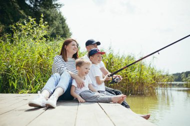 Genç aile, kadın erkek ve iki küçük çocuk gölde balık tutuyor, karı koca birlikte mutlu bir hafta sonu geçiriyorlar.