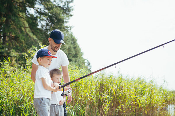 Отец с двумя маленькими сыновьями рыбачит на озере летом по выходным