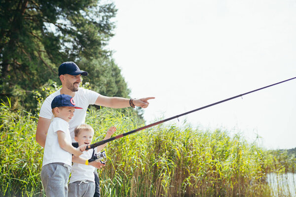Отец с двумя маленькими сыновьями рыбачит на озере летом по выходным