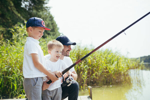 A father with two young sons fishes on the lake in the summer on weekends