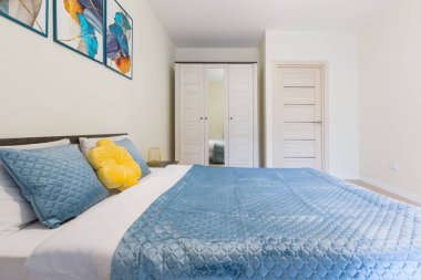Modern minimalist tarzda küçük bir yatak odasının içi, açık renkli, mavi battaniyeli büyük bir yatak.