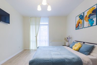 Modern minimalist tarzda küçük bir yatak odasının içi, açık renkli, mavi battaniyeli büyük bir yatak.