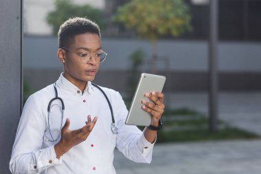 Kadın doktor, elinde bir tablet, kliniğin yanında, personel ile öğle yemeğinde bir konferans bulunan bir video linki ile çevrimiçi konsültasyon gerçekleştiriyor.