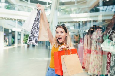 Alışveriş merkezinin üzerinde dans eden neşeli, alışveriş meraklısı, alışveriş torbaları taşıyan ve gülümseyen bir kadın. Kara Cuma 'da eğlenen mutlu kadın, alışveriş merkezinde neşeyle zıplar.