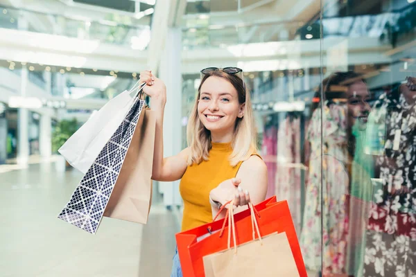 買い物袋を持っている陽気な若いお店の女性は ショッピングセンターで踊るカメラを見て笑っています 幸せな女性持っている楽しいです黒金曜日楽しくジャンプのために喜びでザ モール — ストック写真