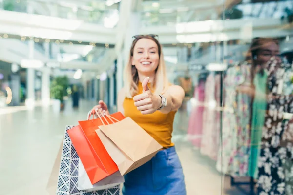 買い物袋を持っている陽気な若いお店の女性は ショッピングセンターで踊るカメラを見て笑っています 幸せな女性持っている楽しいです黒金曜日楽しくジャンプのために喜びでザ モール — ストック写真