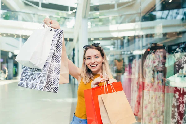 買い物袋を持っている陽気な若いお店の女性は ショッピングセンターで踊るカメラを見て笑っています 幸せな女性持っている楽しいです黒金曜日楽しくジャンプのために喜びでザ モール — ストック写真