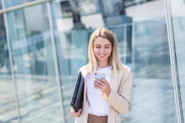 Genç bir iş kadını gider ve elinde cep telefonu kullanır. Şehir geçmişi, modern bir ofis binası. Çekici bir iş kadını ya da öğrenci kadın akıllı telefon kullanarak şehir sokaklarında yürüyor.