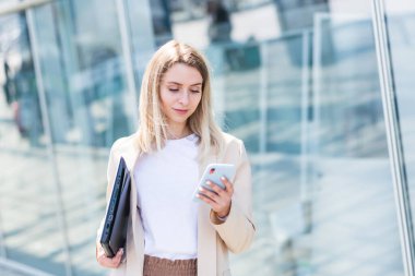 Genç bir iş kadını gider ve elinde cep telefonu kullanır. Şehir geçmişi, modern bir ofis binası. Çekici bir iş kadını ya da öğrenci kadın akıllı telefon kullanarak şehir sokaklarında yürüyor.