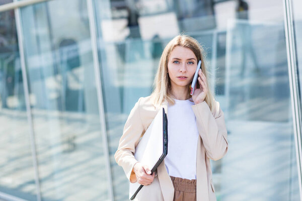 Young beautiful woman talking on a cell phone near the office, a businesswoman on a lunch break