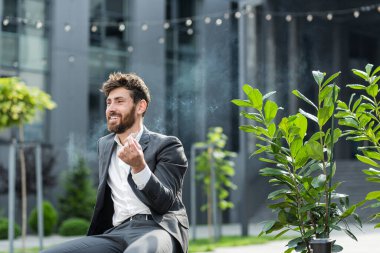 Beyaz sakallı bir iş adamı kenar mahalle arka planında şehir parkındaki bankta esrar içiyor. Erkek işçi, iş adamı. Takım elbiseli bir ofis çalışanı dışarıda bir marihuanayı rahatlatıyor.