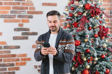 Ciddi ve odaklanmış bir adam evdeki Noel ağacının yakınındaki bir cep telefonuyla mektuplaşıyor.