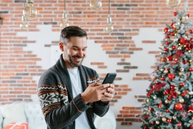 Adam gülümsüyor ve internet başvurularındaki arkadaşlarıyla yeni yıl ve Noel tatillerinde yazışmak için bir cep telefonu kullanıyor.