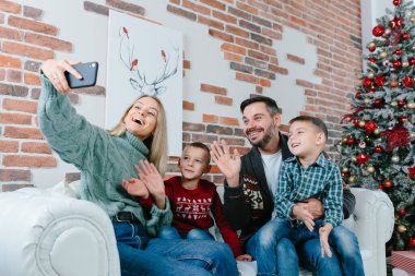 İki çocuklu, mutlu, güzel bir evli çift arkadaşlarıyla ya da aileleriyle telefonda konuşurken video konferans uygulaması ile mutlu Noeller diliyor. Modern teknoloji Yeni Yıl 2022 Tebrikler.