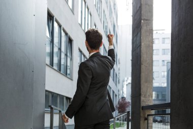 Başarılı Kafkasyalı işadamı kollarını kaldırıp zaferi kutluyor. Kavram: başarı, kariyer gelişimi, zafer, özgürlük. Modern bir ofis binasının arka planında çalışan siluet işadamı. dışarıName