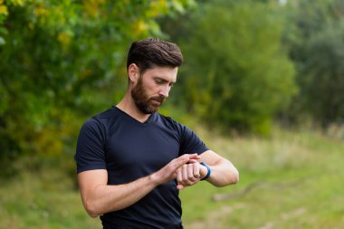 Modern hipodrom koşucusunda akıllı görünümlü beyaz bir adam. Akıllı spor bilekliği kullanıyor. Portre formalı erkek sporcu.