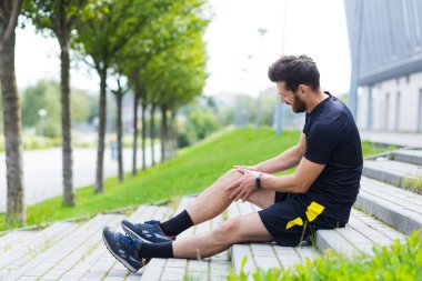 Sporcu erkek antrenman sırasında yaralanmış, şiddetli bacak ağrısı, kas ağrıları var, yerde oturuyor ve acı içinde bağırıyor.