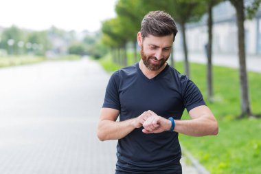 Modern hipodrom koşucusunda akıllı görünümlü beyaz bir adam. Akıllı spor bilekliği kullanıyor. Portre formalı erkek sporcu.