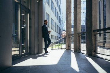 Ofise yakın bir erkek işadamı, tablet bilgisayardan haberleri okuyor. Ofisin dışında takım elbiseli, Afro-Amerikan bir serbest yazar.
