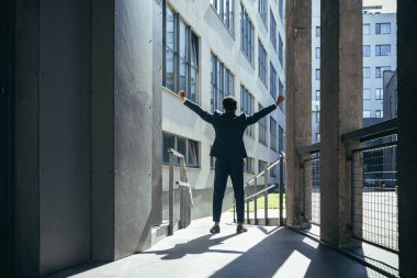 Başarılı Afro-Amerikan iş adamı zafer kutlaması yapıyor. Kavram: başarı, kariyer gelişimi, zafer, özgürlük. Arka planda, modern bir ofis binasının silueti olan bir iş adamı. dışarıName