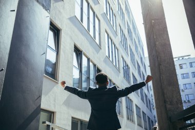 Başarılı Afro-Amerikan iş adamı zafer kutlaması yapıyor. Kavram: başarı, kariyer gelişimi, zafer, özgürlük. Arka planda, modern bir ofis binasının silueti olan bir iş adamı. dışarıName