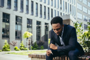 Afro-Amerikan iş adamı kenevir içiyor şehir parkındaki bankta oturuyor. Erkek işçi, iş adamı. Takım elbiseli bir ofis çalışanı dışarıda bir marihuanayı rahatlatıyor.