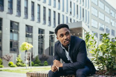 Afro-Amerikan iş adamı kenevir içiyor şehir parkındaki bankta oturuyor. Erkek işçi, iş adamı. Takım elbiseli bir ofis çalışanı dışarıda bir marihuanayı rahatlatıyor.