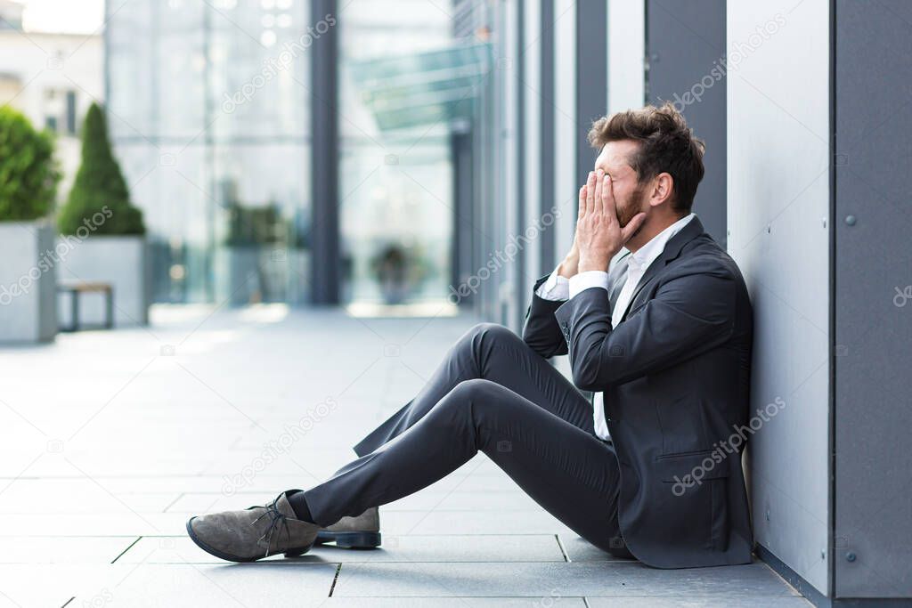 Depressed bankrupt man crying near office outdoors, lost his job and hope