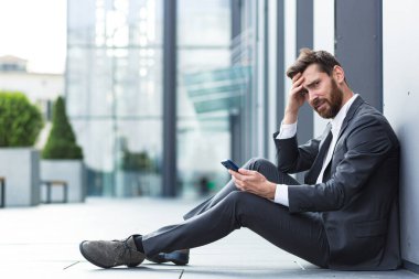 Ofis çalışanı dışarıda otururken kötü haberler aldı, depresif ve yorgun internet üzerinden kötü haberler okuyor.