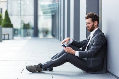 Ofis çalışanı dışarıda otururken kötü haberler aldı, depresif ve yorgun internet üzerinden kötü haberler okuyor.