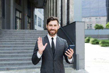 Resmi takım elbiseli sakallı iş adamı, şehir sokaklarındaki kendine güvenen iş adamı, girişimci ya da çalışan konuşmalarında akıllı telefon kullanarak görüntülü konuşma yapan cep telefonu geçmişi olan modern merkez.