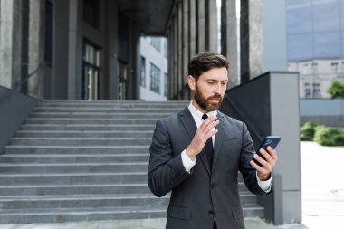Resmi takım elbiseli sakallı iş adamı, şehir sokaklarındaki kendine güvenen iş adamı, girişimci ya da çalışan konuşmalarında akıllı telefon kullanarak görüntülü konuşma yapan cep telefonu geçmişi olan modern merkez.