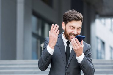 Kızgın erkek işadamı dışarıda telefonda konuşurken ağlıyor. Dışarıdaki çağrıda bağırıyor. Akıllı telefondan sinirli, profesyonel bir konuşma. Sinirli çalışan çığlığı Kentsel caddede konuşuyor.