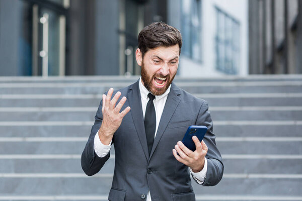 angry male businessman cry talking on the phone outside business man shouting on call outdoors. Nervous mad professional conversation on smartphone. Irritated employee scream speak at urban street