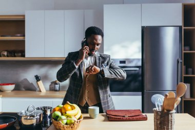 Afro-Amerikalı iş adamı evde çalışıyor, mutfakta kahvaltı yapıyor, telefonda konuşuyor.
