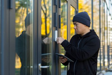 Erkek hırsız bir virüs programıyla evdeki alarmı kırmaya çalışıyor, tablet kullanıyor, Asyalı.