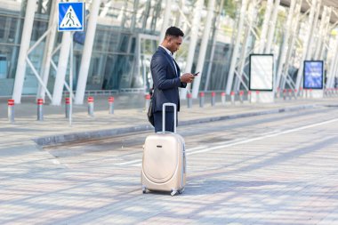 Başarılı genç, kendinden emin Afro-Amerikan iş adamı cep telefonuyla modern ofis arka planına karşı hareket ediyor. Siyah iş adamı resmi takım elbise içinde cep telefonuyla yürüyor.