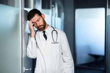 Yorgun doktor çok çalışıyor, başı çok ağrıyor, kötü hissediyor, kliniğin koridorundaki bir adam sonuçtan hayal kırıklığına uğruyor.