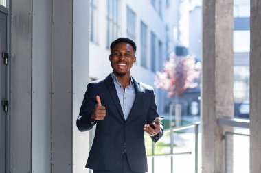 Başarılı Afro-Amerikan iş adamı gülümser ve kameraya bakar, Happy telefonu kullanır ve parmağını kaldırmaz.