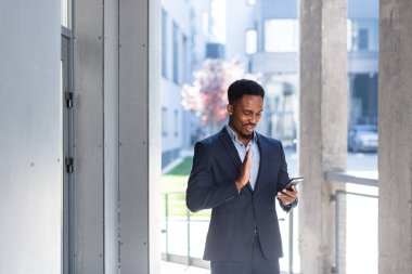 Video görüşmesi yapan Afro-Amerikalı işadamları ofis dışında telefon ve uygulama kullanıyor. Takım elbiseli, neşeli ve başarılı bir adam.