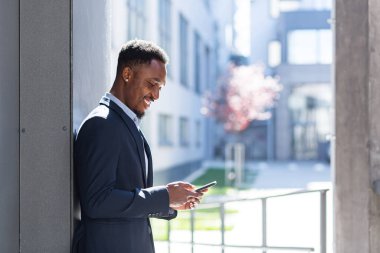 Başarılı ve mutlu Afro-Amerikan iş adamı elinde cep telefonu gülümsemesi ve sevinçle haberleri okuyor ve yazıyor.
